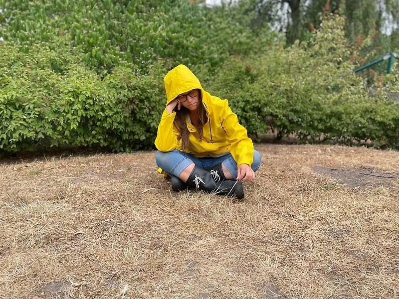 Person i gul regnjacka sitter på brunbränt gräs
