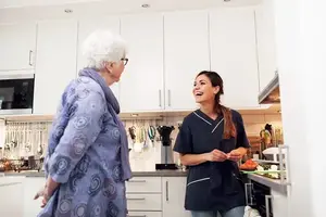 Hemtjänstpersonal i köket samspråkar med äldre kvinna